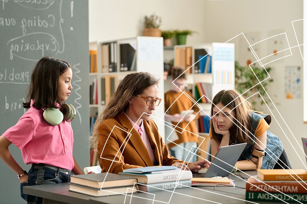 Profesora y alumnas trabajan con portátiles y libros en un aula conectada